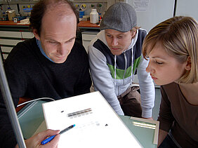 Biochemie-Professor Utz Fischer betrachtet mit den Biologie-Diplomanden Georg Stoll und Lisa Buckel das Ergebnis einer Protein-Trennung. Solche Analysen sind ein wichtiger Teil der biochemischen Forschung. Foto: Robert Emmerich