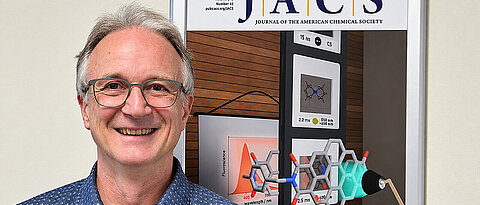 Porträtfoto von Frank Würthner vor einem Poster