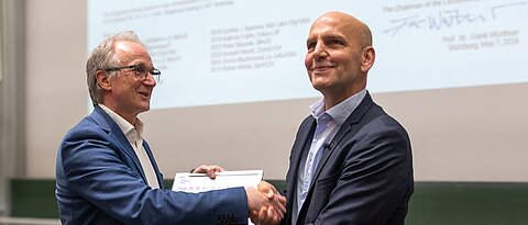 Der Moment der Urkundenüberreichnung durch Frank Würthner an Benjamin List im Hörsaal B