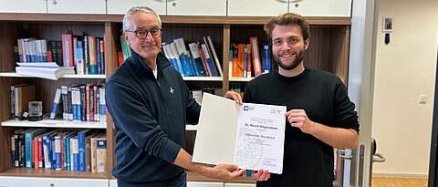 Alexander Bausback erhält die Stipendienurkunde von Professor Dr. Christoph Lambert in dessen Büro